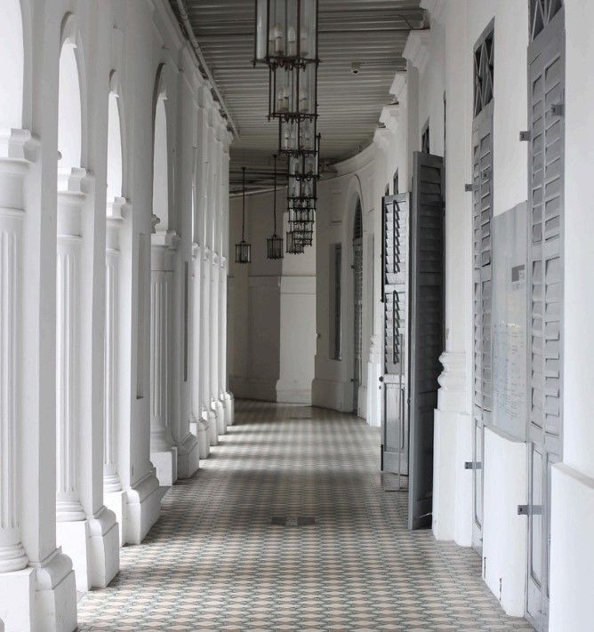 Pasillo largo con columnas blancas, suelo de baldosas y lámparas colgantes.