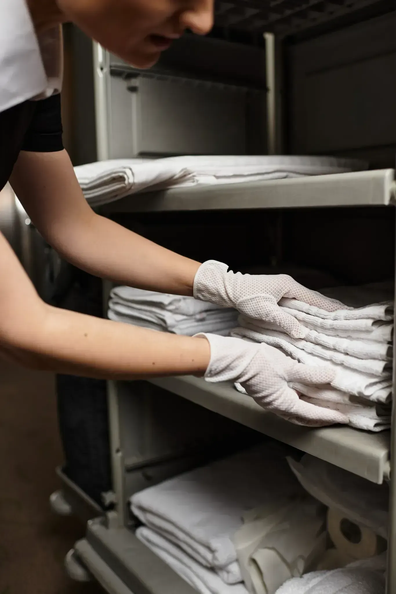 Persona con guantes, colocando toallas blancas dobladas en un carrito de hotel.
