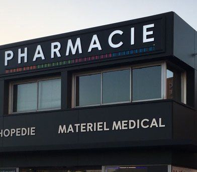Enseigne Pharmacie blanche sur fond noir avec une bande colorée au-dessus