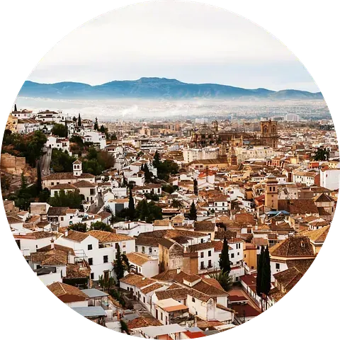 Paisaje urbano de Granada, España, con edificios blancos, techos de terracota y montañas al fondo.