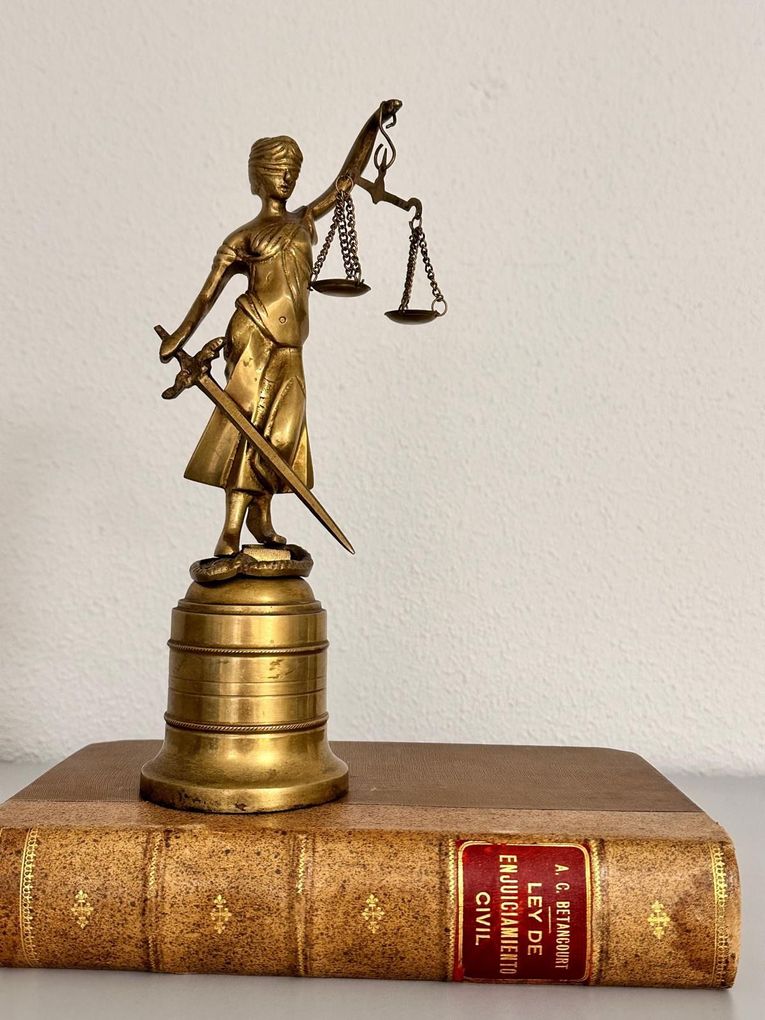 Estatua de la Dama de la Justicia sosteniendo una balanza y una espada encima de un libro.