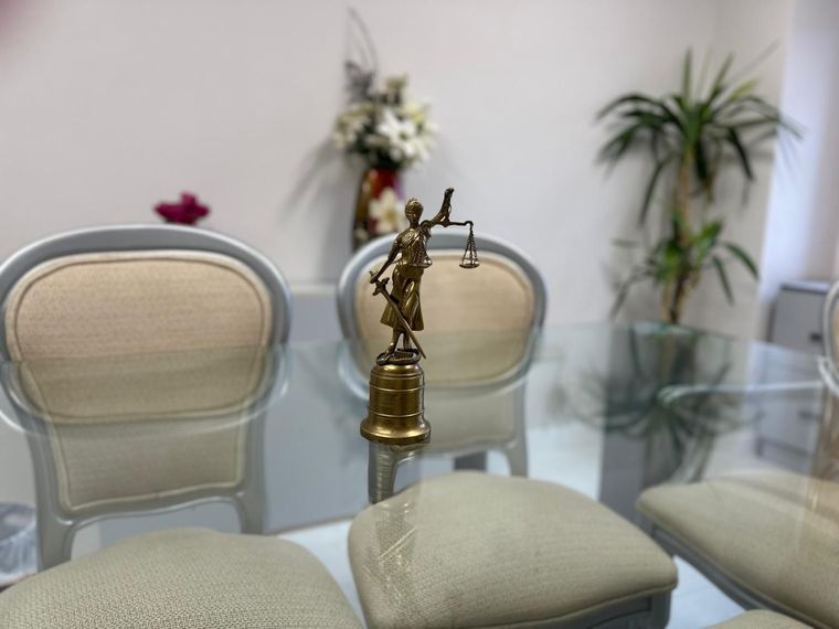 Figura de Lady Justice sobre una mesa de cristal en un entorno de oficina con sillas y plantas.