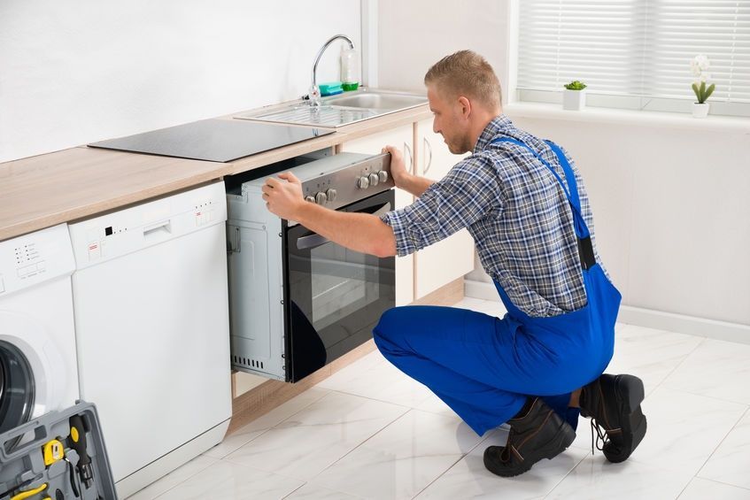 Un hombre está arreglando un horno en una cocina.