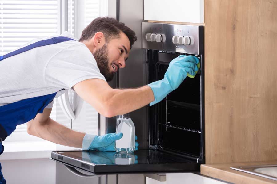 Un hombre está limpiando un horno en una cocina.