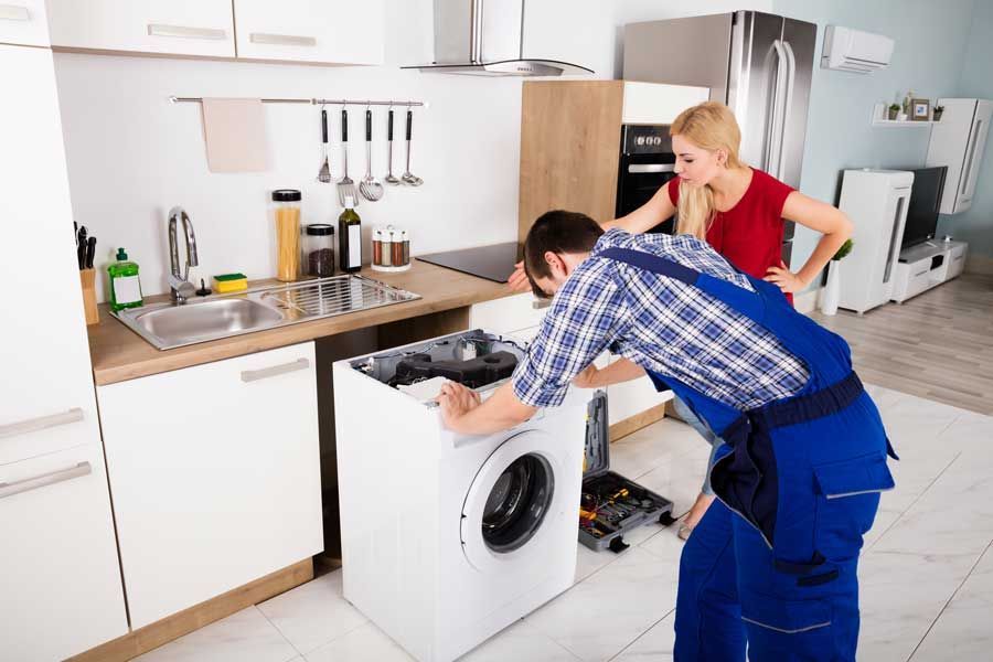 Un hombre está arreglando una lavadora en una cocina mientras una mujer observa.