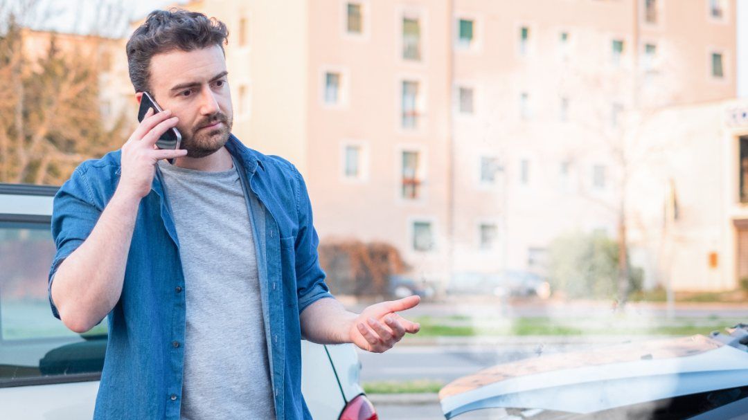 Un hombre está hablando por un teléfono celular mientras está parado al lado de un automóvil.