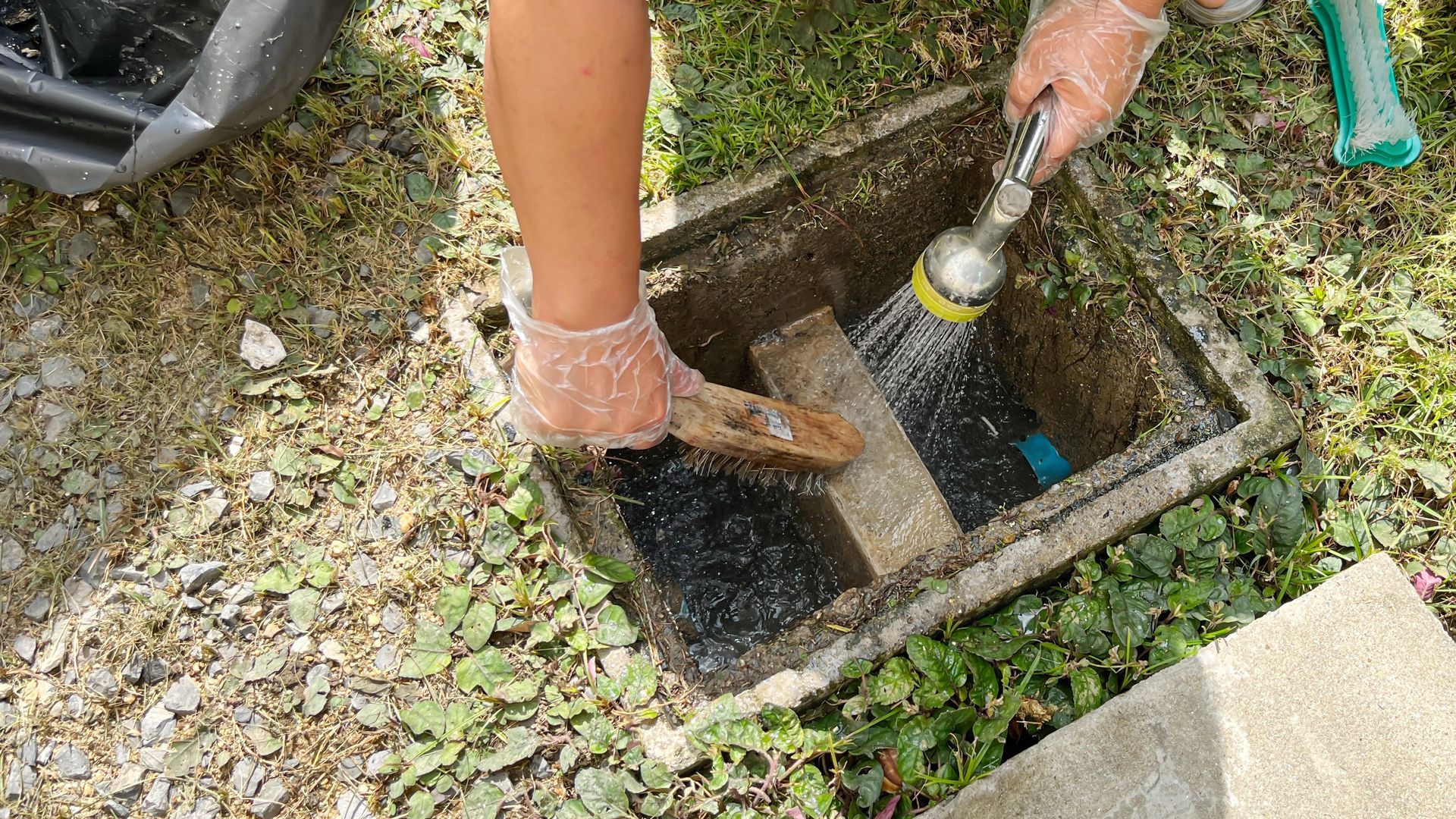 Une personne en train de nettoyer un bac à graisse avec un jet d'eau.