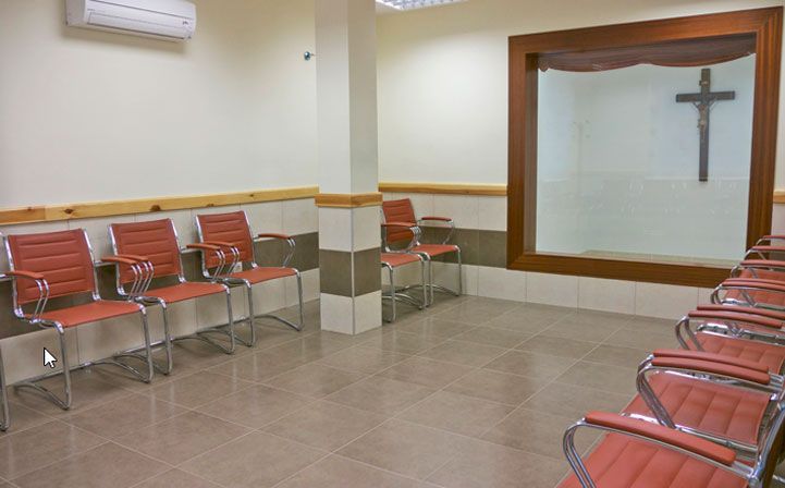 Una sala de espera con sillas y una cruz en la pared.