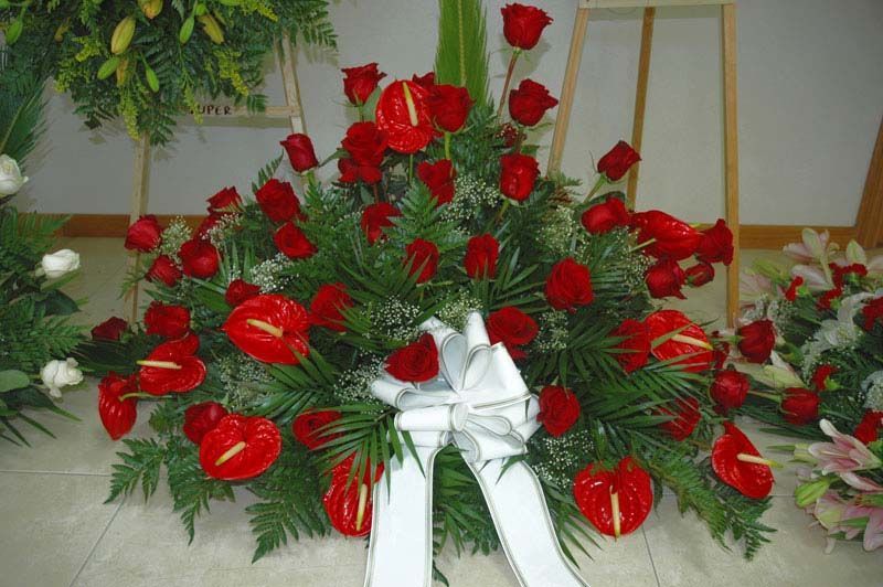 Un ramo de rosas rojas y anturios con un lazo blanco.