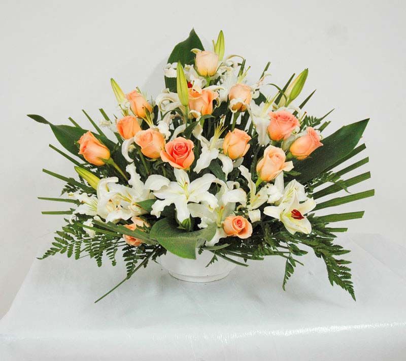 Un jarrón lleno de flores, incluidas rosas y lirios.
