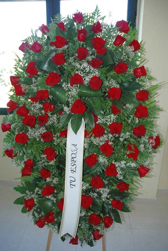 Una corona de rosas rojas con una cinta que dice tu espola