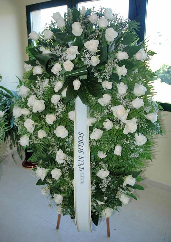 Una corona de rosas blancas con una cinta que dice tus brazos