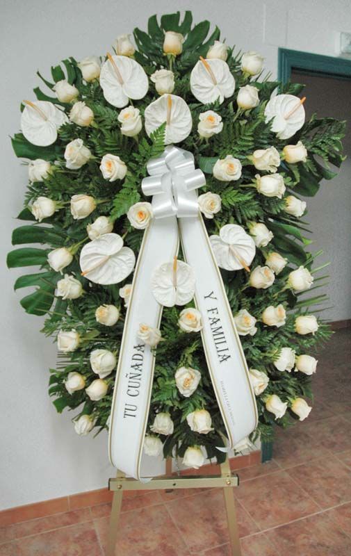 Una corona de rosas blancas con una cinta blanca que dice