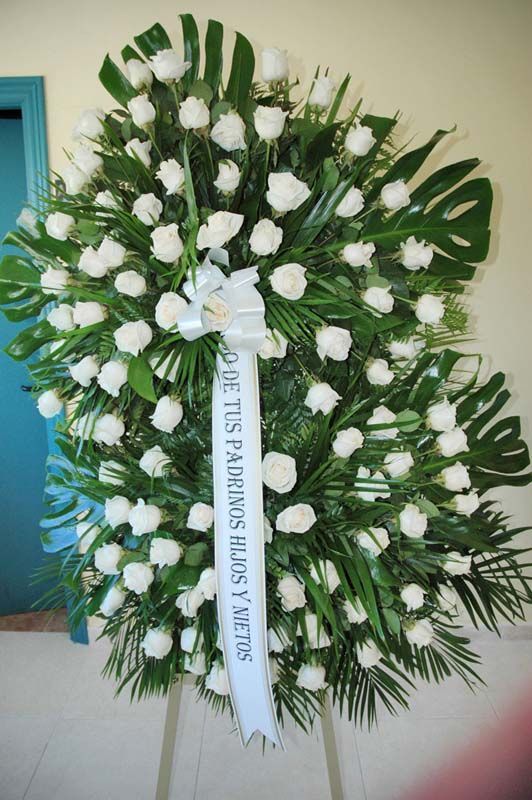 Una corona de rosas blancas con una cinta que dice