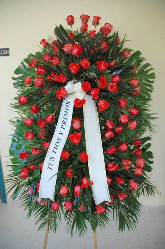 Una corona con rosas rojas y una cinta blanca que dice tus tres y primos