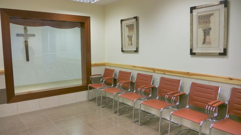 Una sala de espera con sillas y una cruz en la pared.