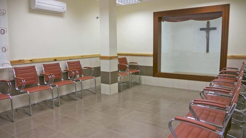 Una sala de espera con sillas y una cruz en la pared.