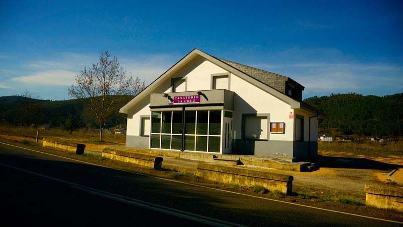 Un pequeño edificio blanco con un cartel morado está situado al costado de una carretera.