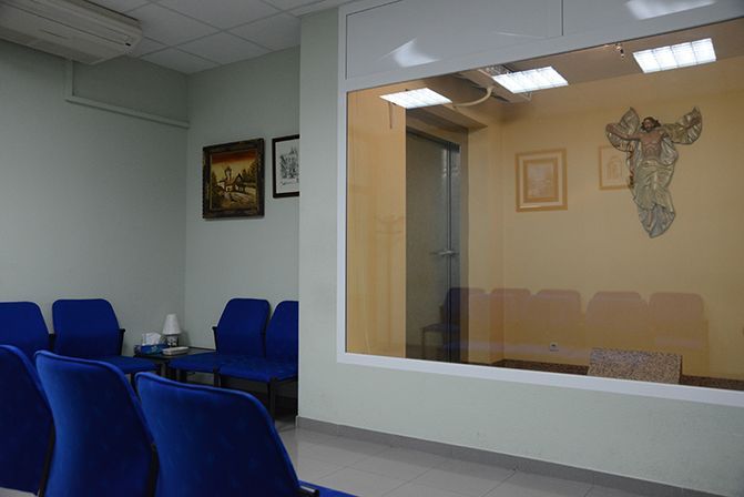 Una sala de espera con sillas azules y una cruz en la pared.