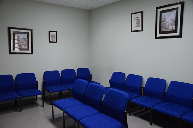 Una sala de espera con sillas azules y cuadros en la pared.