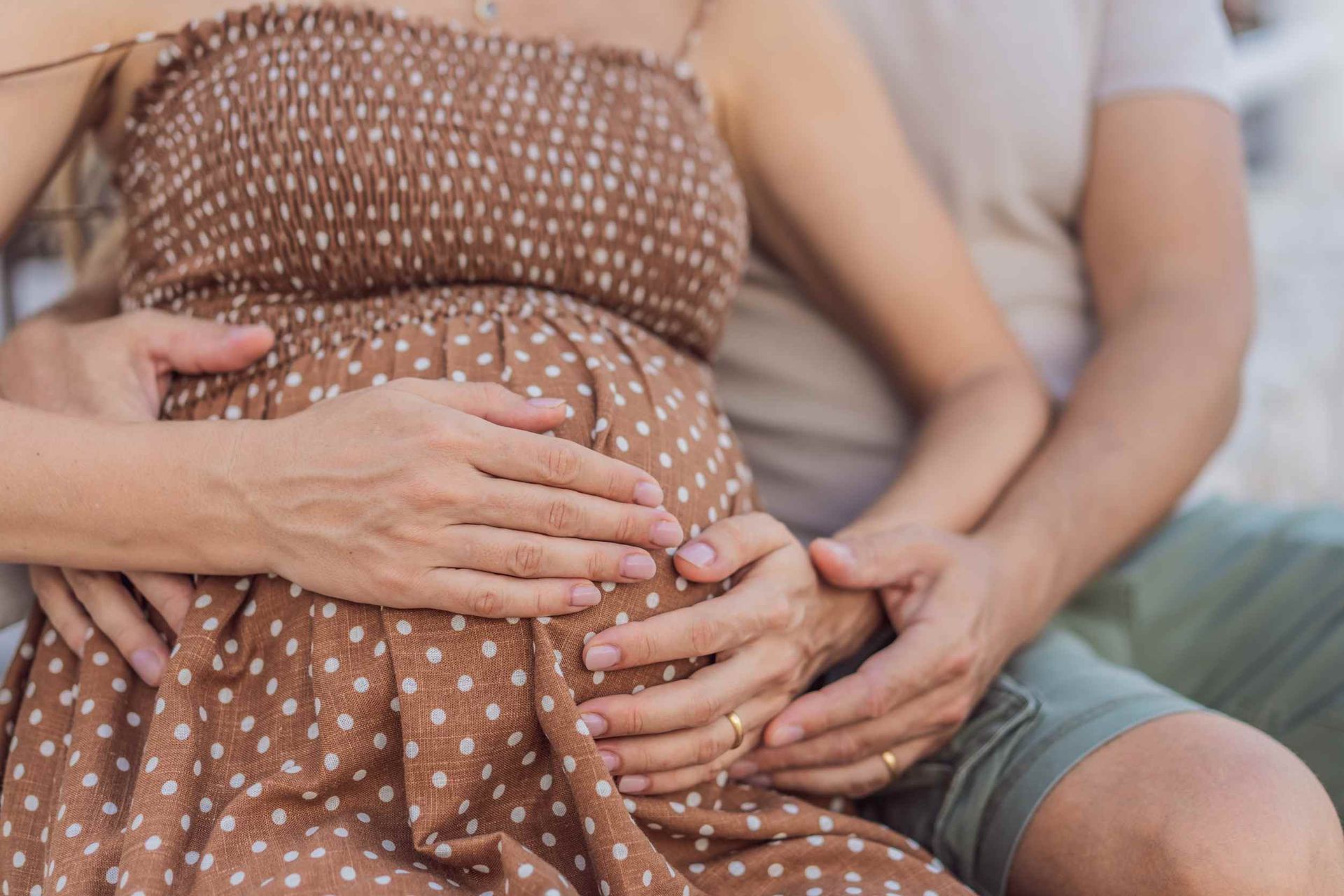 Una mujer embarazada está sentada junto a un hombre que sostiene su vientre.