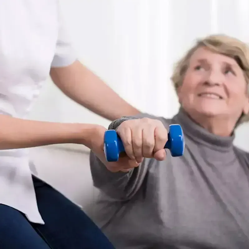 Una mujer está ayudando a una anciana a levantar una mancuerna azul.