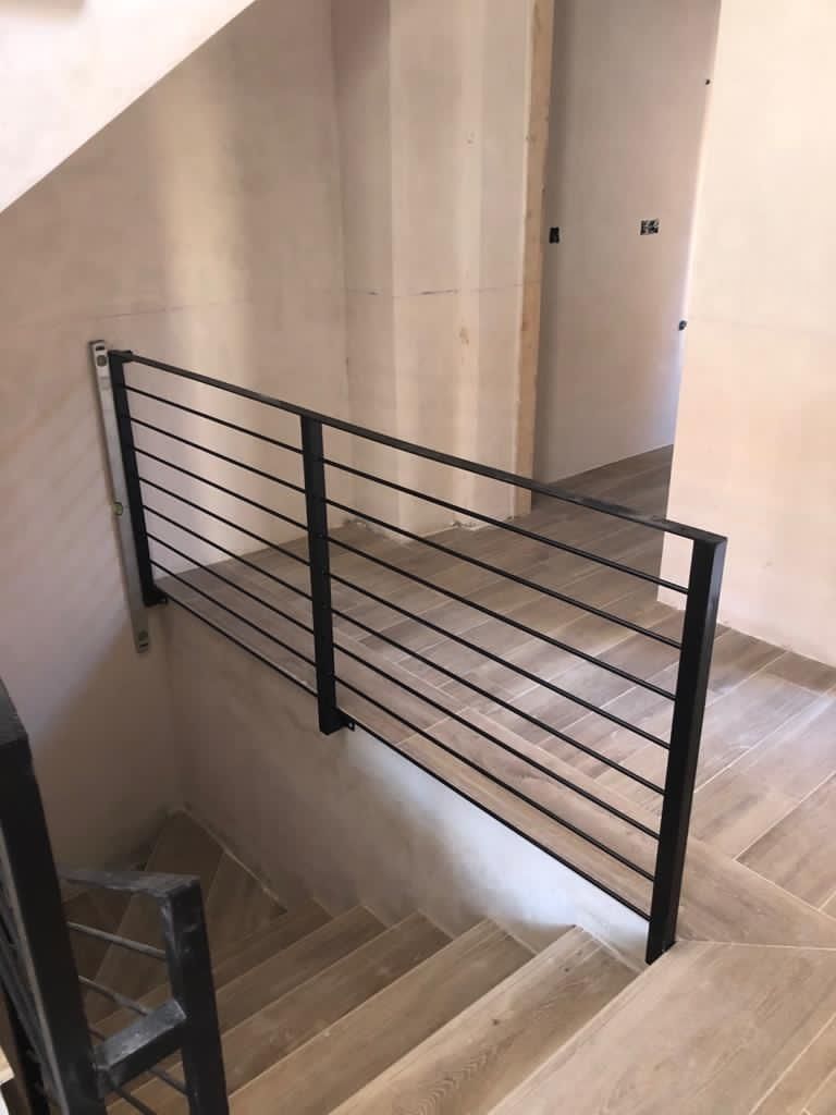 Una escalera con barandilla negra y escalones de madera.