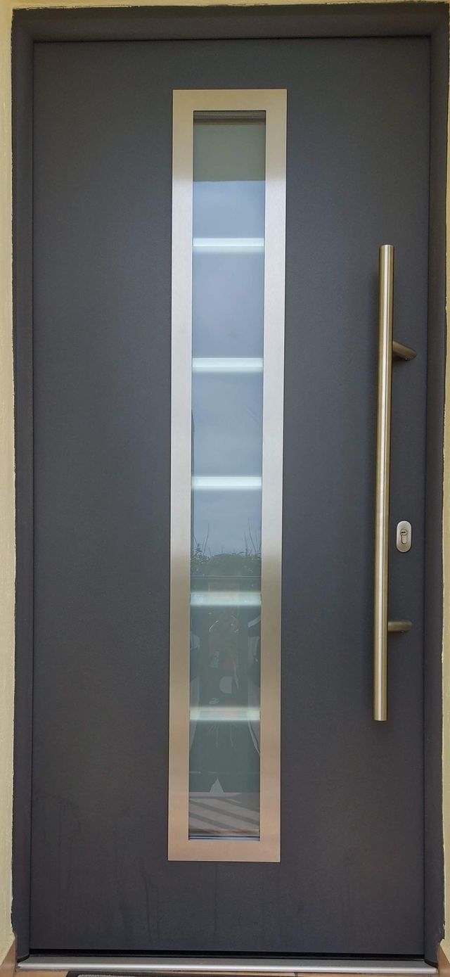 Una puerta negra con manija de acero inoxidable y una ventana.