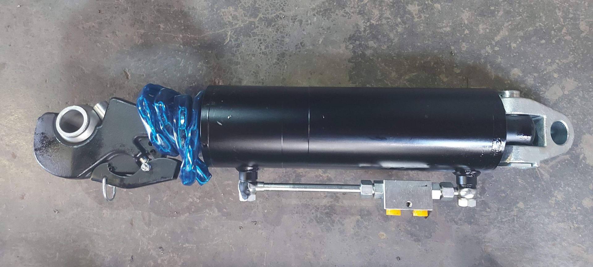 Un cilindro hidráulico negro está asentado sobre una superficie de hormigón.