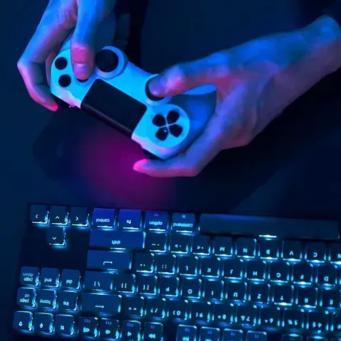 Una persona sostiene un controlador de videojuego frente a un teclado.