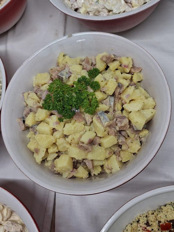 Bol de salade de pommes de terre en dés garni de persil, avec d'autres plats partiellement visibles autour.