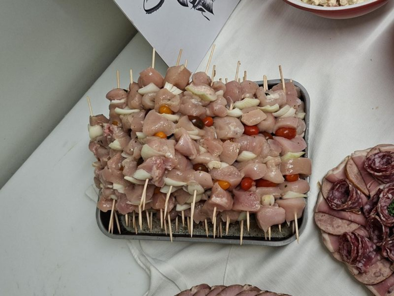 Plateau de brochettes de viande crue et de légumes sur une table, avec des oignons émincés et d'autres plats à proximité.