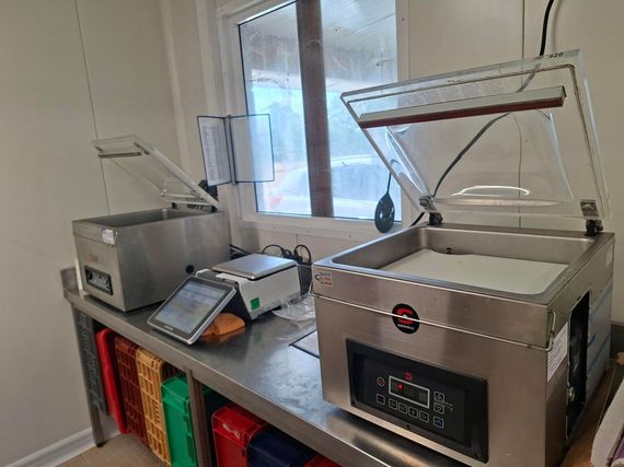 Comptoir de préparation alimentaire commercial avec deux machines en acier inoxydable, une tablette et des bacs colorés en dessous.