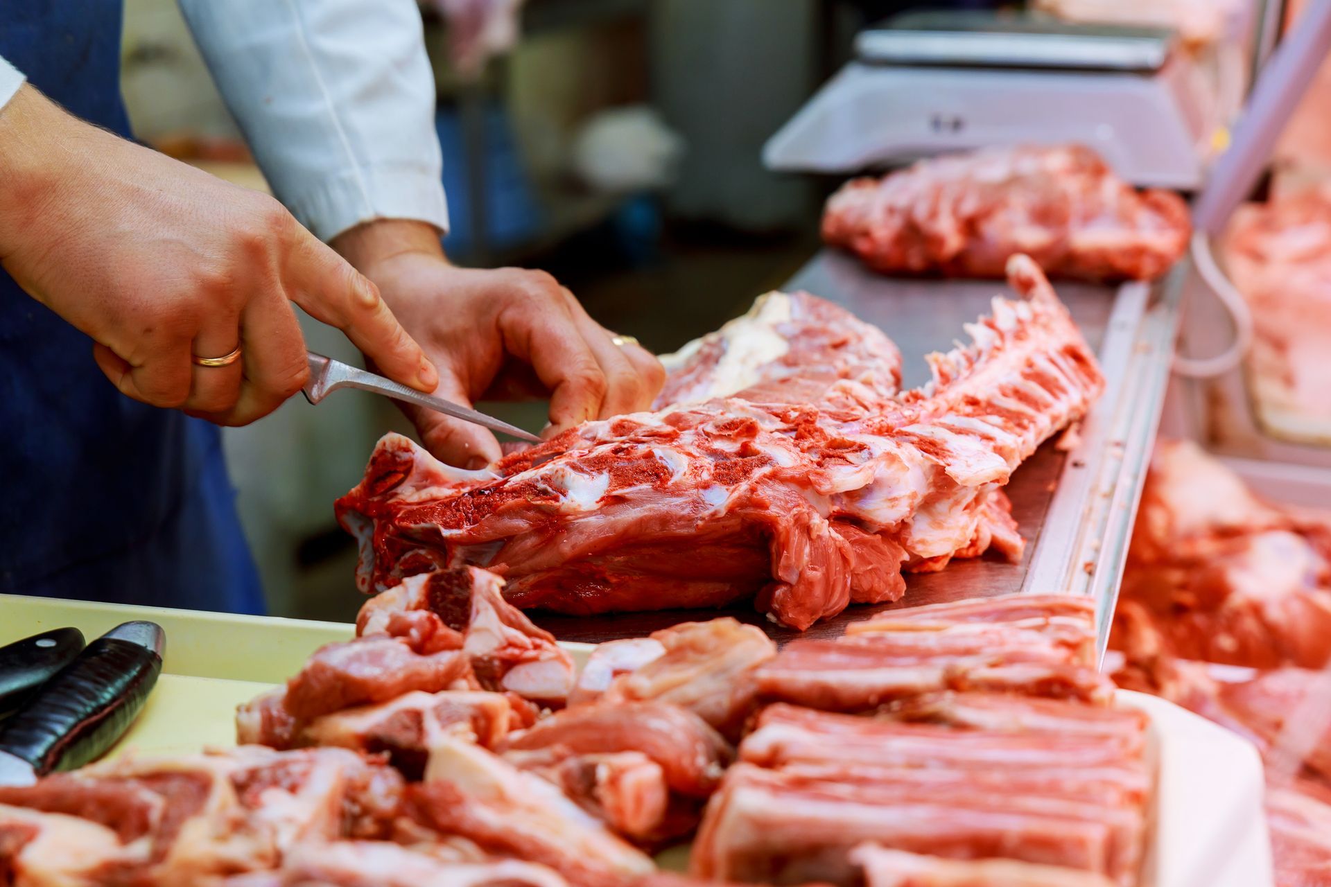 Un boucher découpe de la viande crue sur un étal de marché, des côtes et des morceaux de viande empilés sur un plateau.