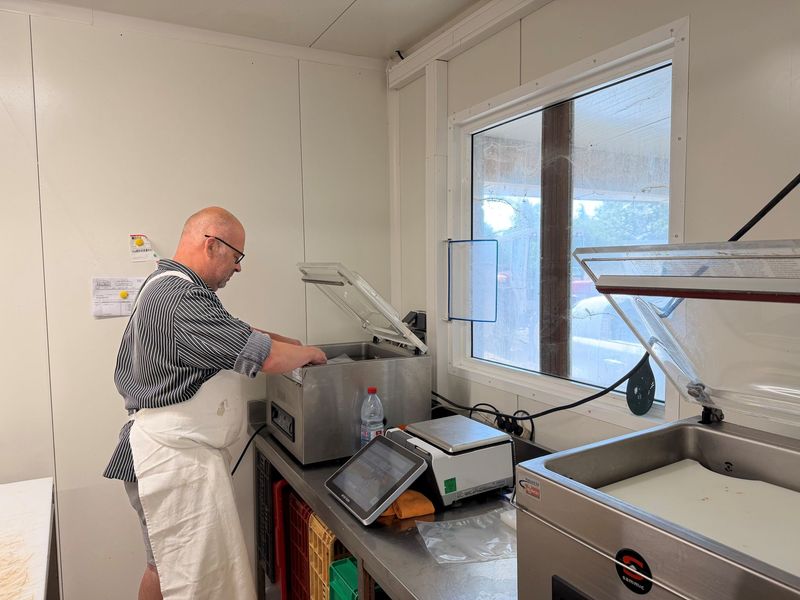Plateaux de viande crue dans une salle de transformation alimentaire, avec des ouvriers en arrière-plan.