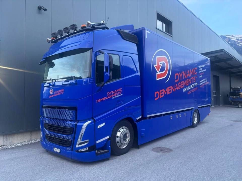 Une camionnette de livraison bleue est garée à côté d'un entrepôt, avec le logo « Dynamic Deliveries » sur le côté.