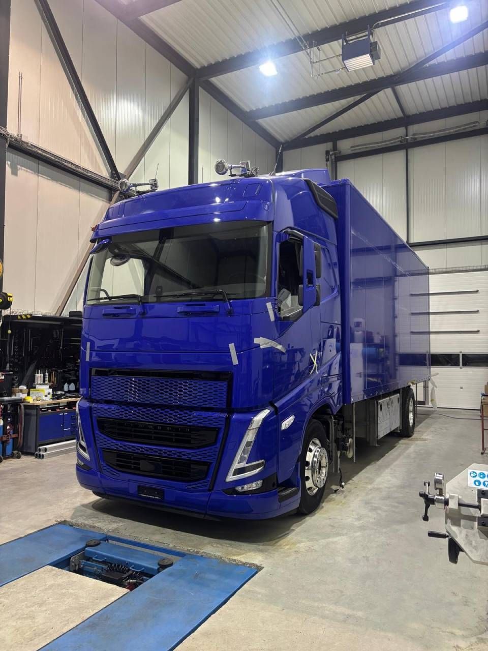 Un camion bleu est garé dans un garage-entrepôt aux hauts plafonds, avec des outils à proximité.