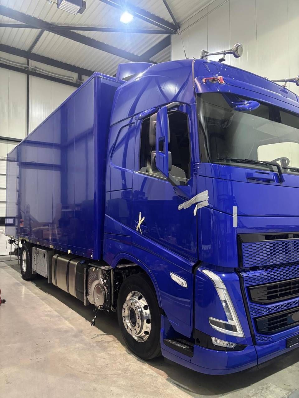 Un semi-remorque bleu avec une remorque fourgon est stationné dans un garage d'entrepôt.
