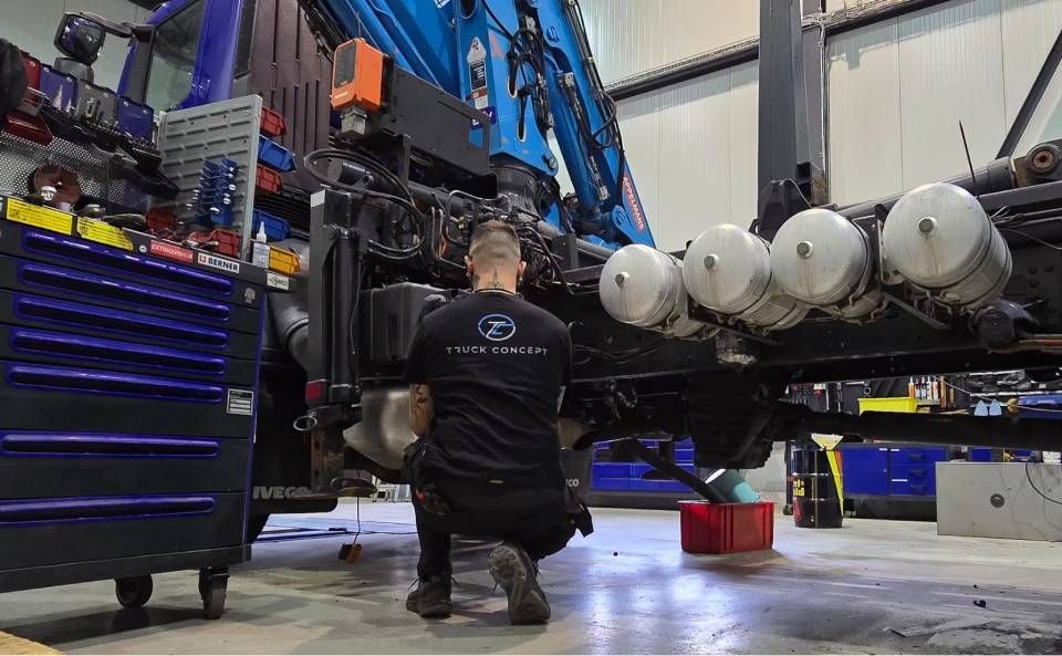 Un ouvrier agenouillé à côté d'un grand ensemble de machines avec une structure bleue et des cylindres.
