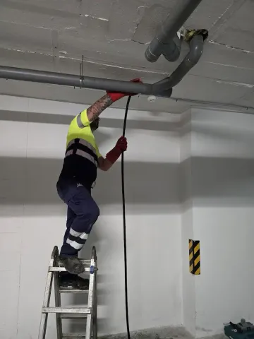 Trabajador subido a una escalera pintando o reparando una tubería del techo en un estacionamiento.