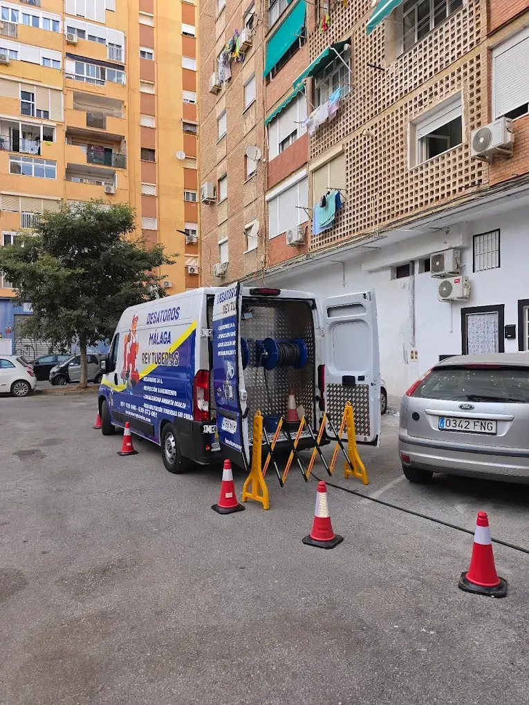 Un trabajador en una furgoneta azul coloca conos junto a edificios de apartamentos en una calle.