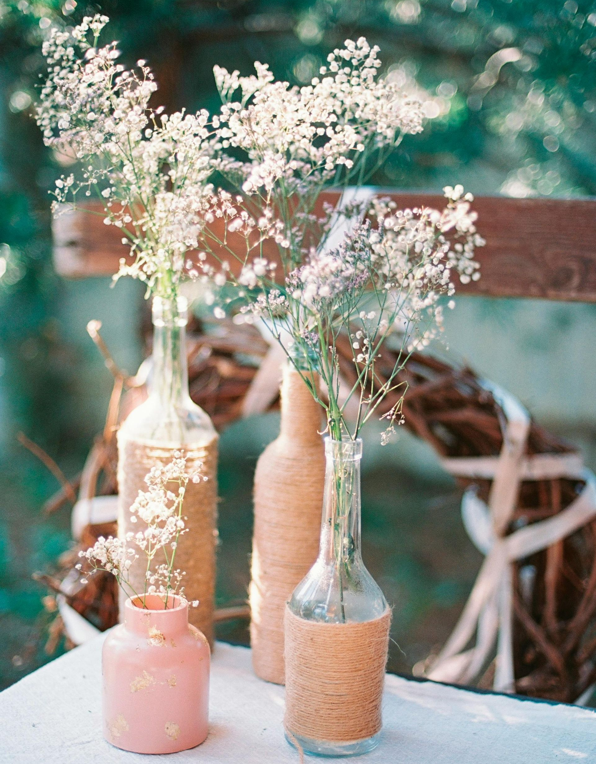 Vasen mit Schleierkraut auf einem Tisch. Einige Vasen sind mit strukturiertem Papier umwickelt. Draußen, unscharfer Hintergrund.