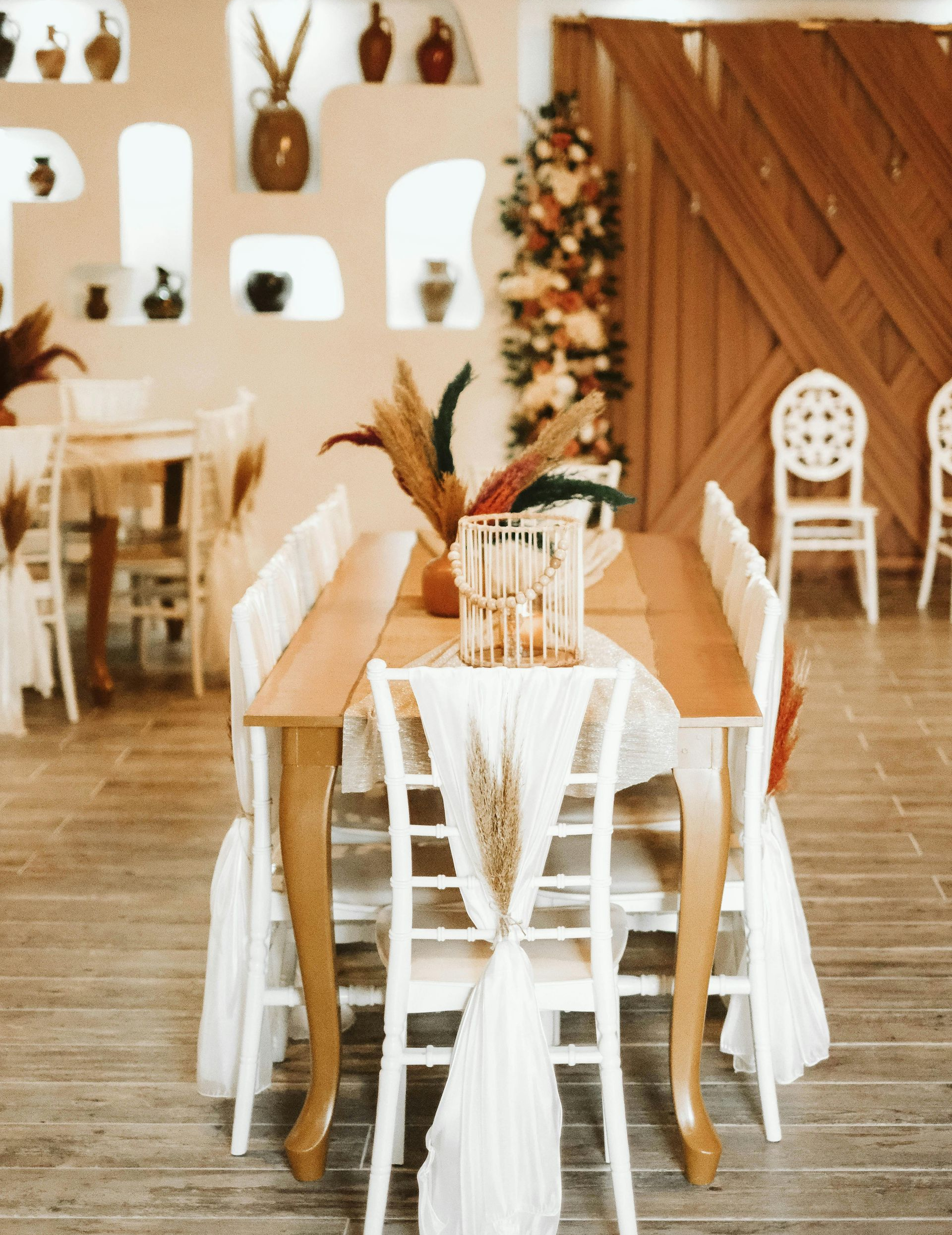 Ein für eine Veranstaltung gedeckter Esstisch mit weißen Stühlen, Holzelementen und dekorativen Accessoires.