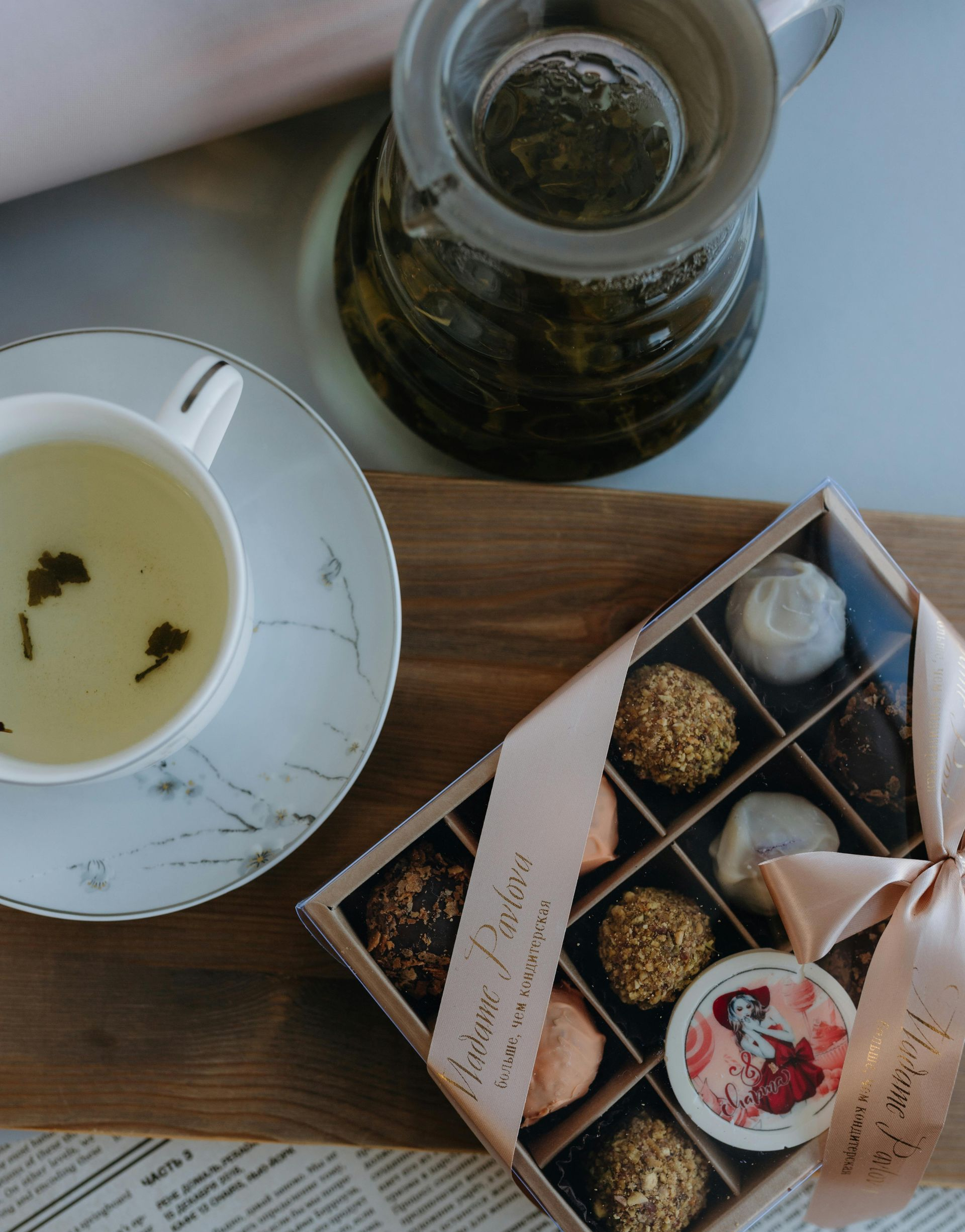 Eine Tasse Tee, eine Teekaraffe und eine Schachtel Pralinen auf einer Holzoberfläche.