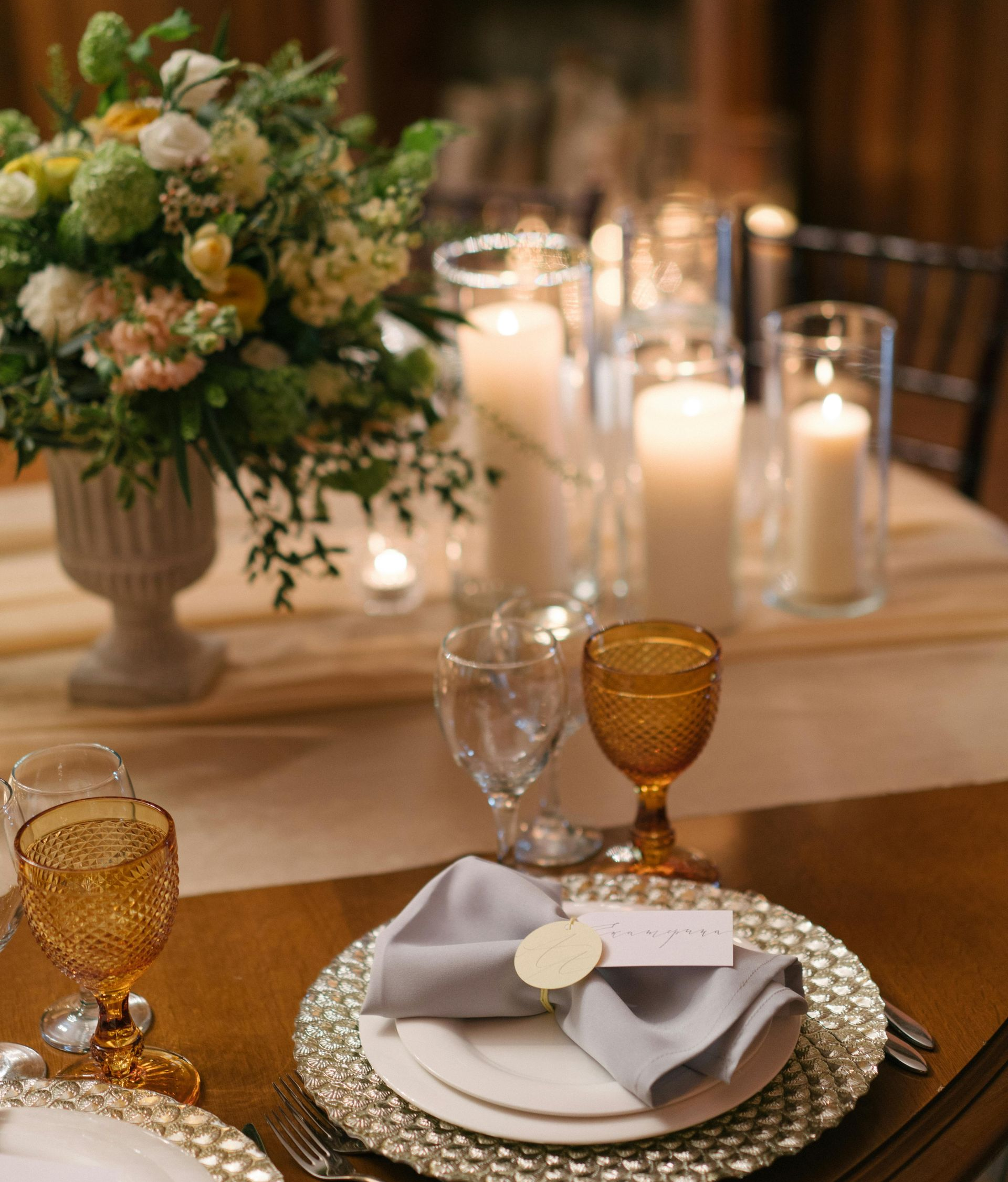 Elegant gedeckter Tisch mit Blumenarrangement, Kerzen und bernsteinfarbenen Gläsern.