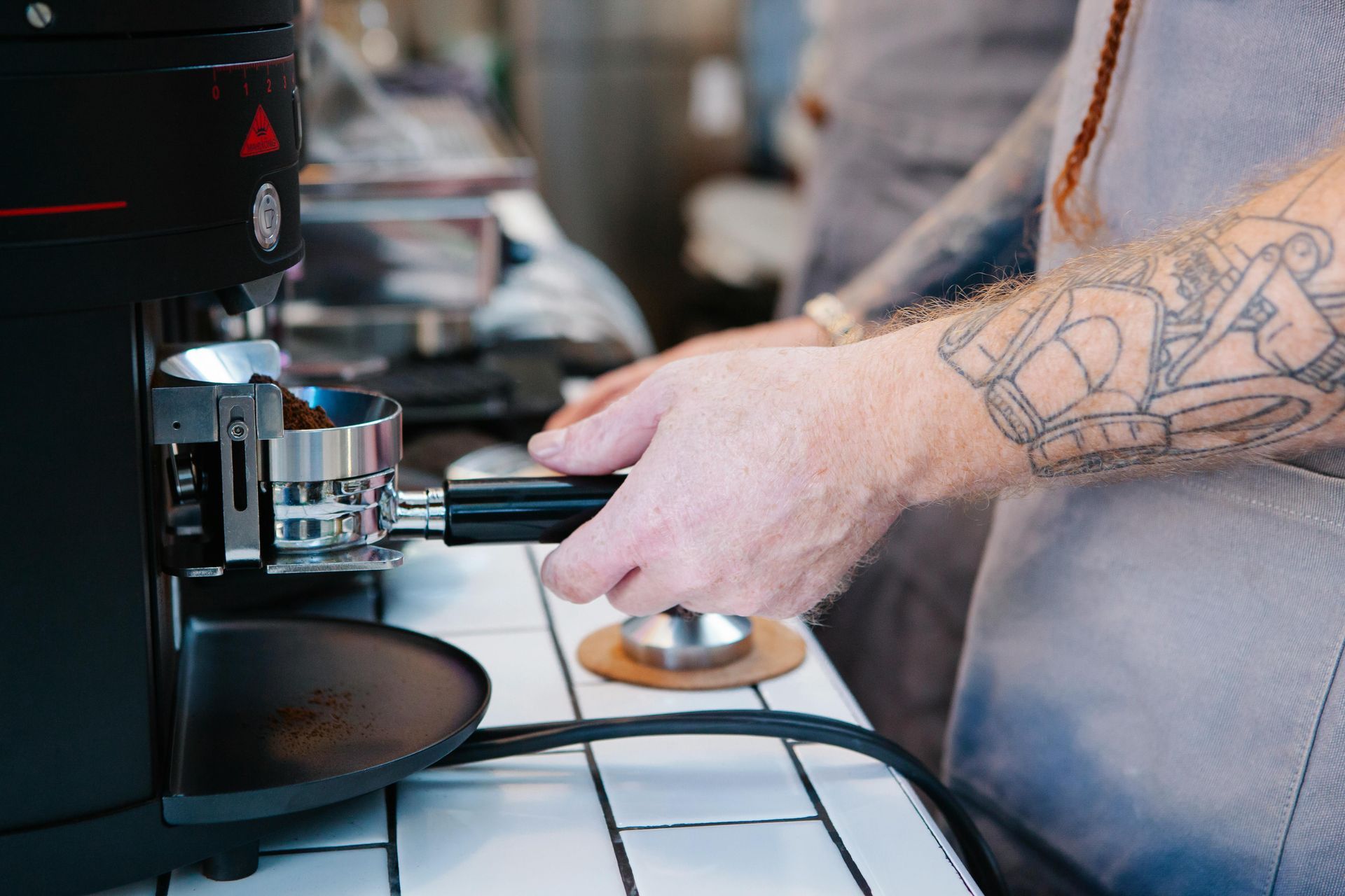 Ein Barista mahlt Kaffeebohnen mit einer elektrischen Kaffeemühle in einen Siebträger.