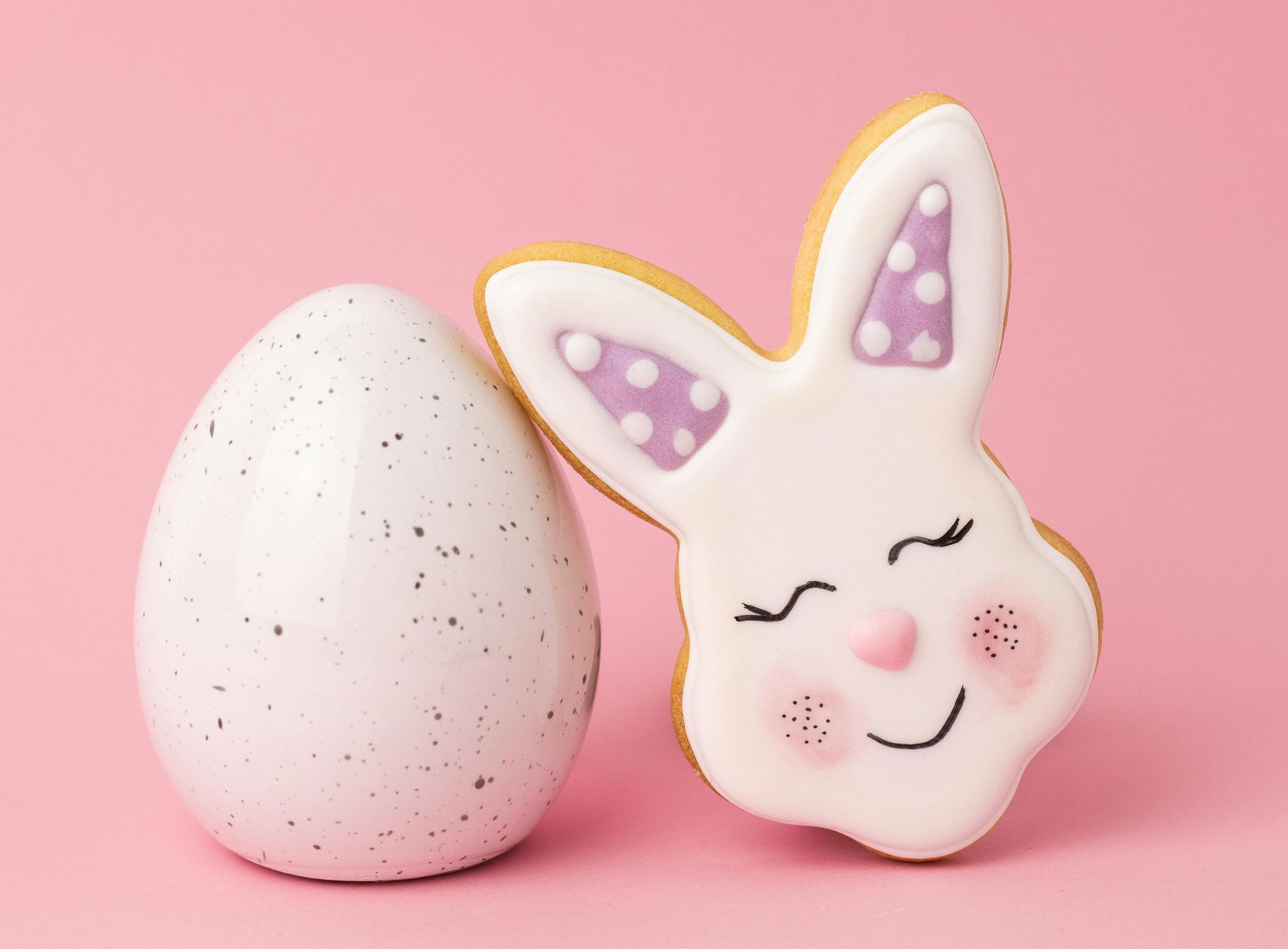 Weißes, gesprenkeltes Ei und Hasenkeks mit rosa Akzenten auf rosa Hintergrund.