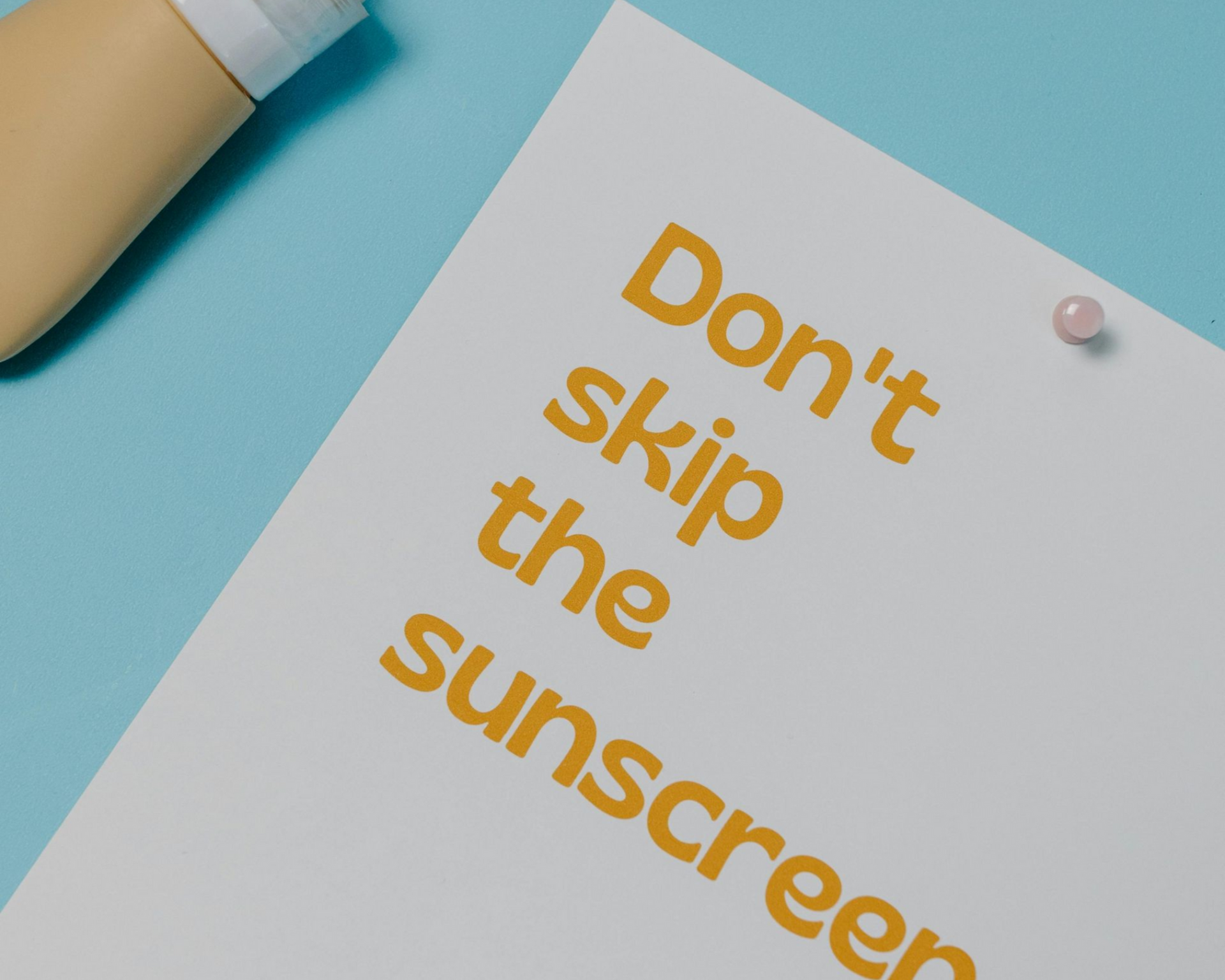 Sunscreen bottle, torn paper strips, and a note reading “Don’t skip the sunscreen” on a blue background