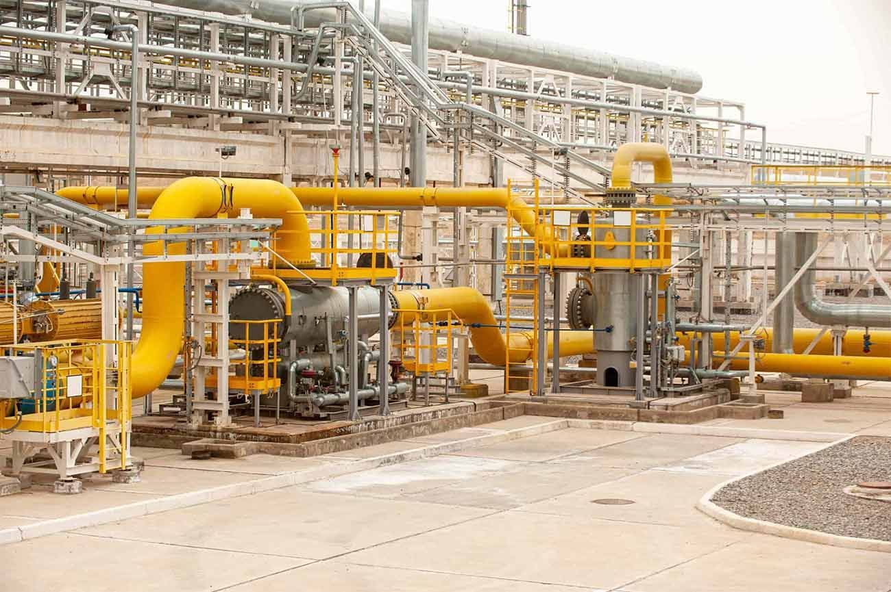 Planta industrial con grandes tuberías amarillas y estructuras de acero en una instalación exterior polvorienta.