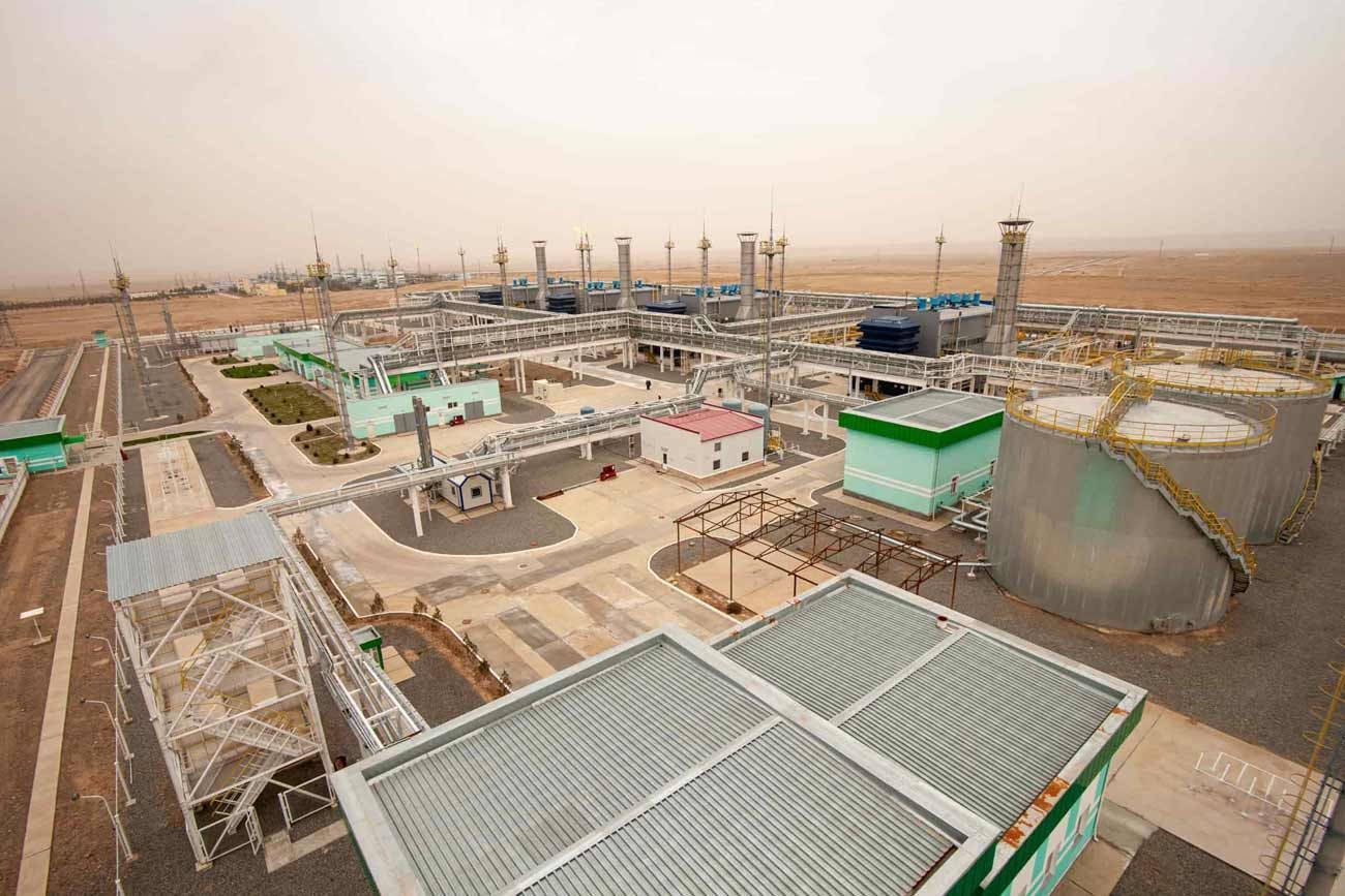 Planta industrial con grandes tanques, tuberías y torres en un entorno desértico polvoriento.